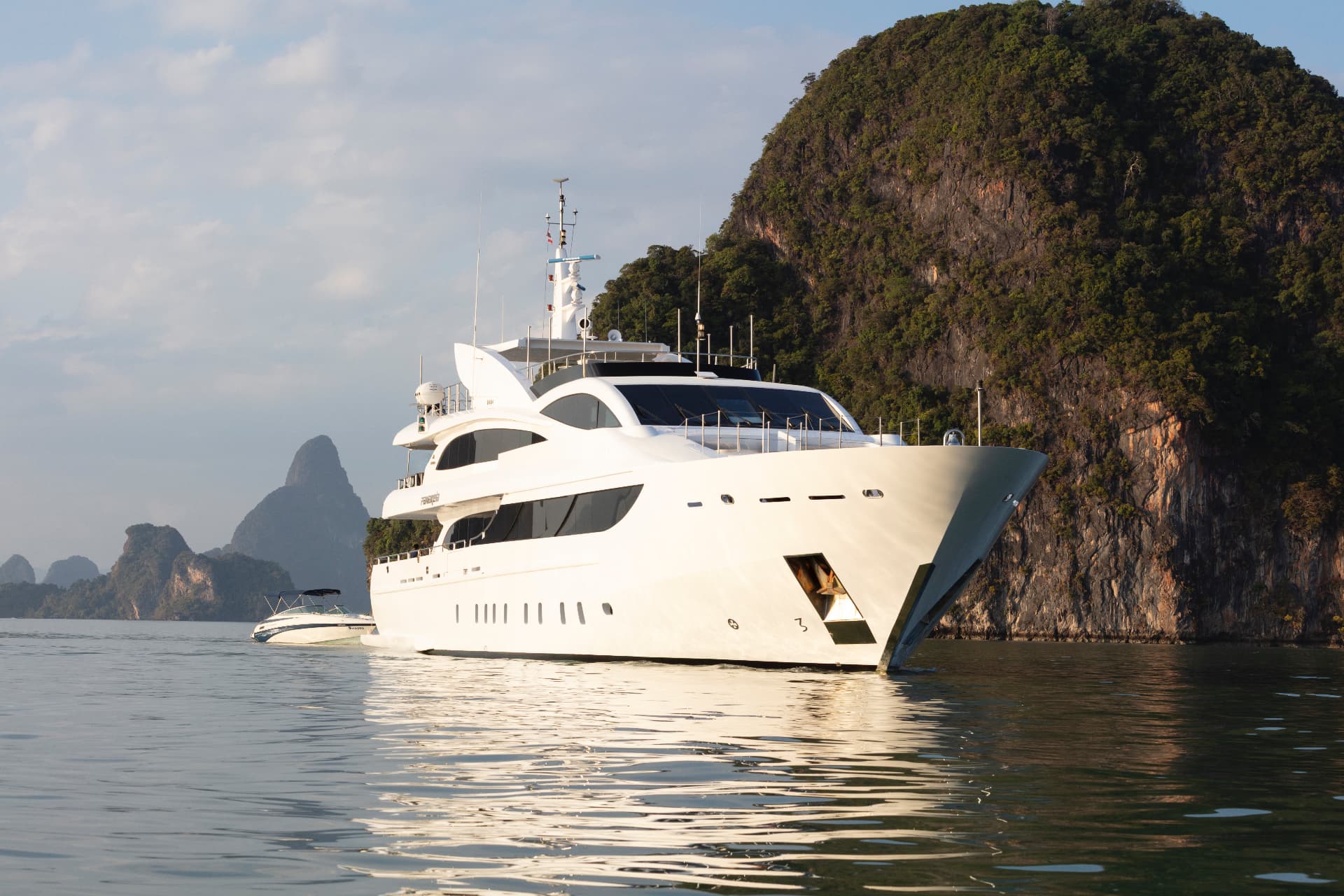 Phuket superyacht charter anchored beside dramatic island cliffs at golden hour